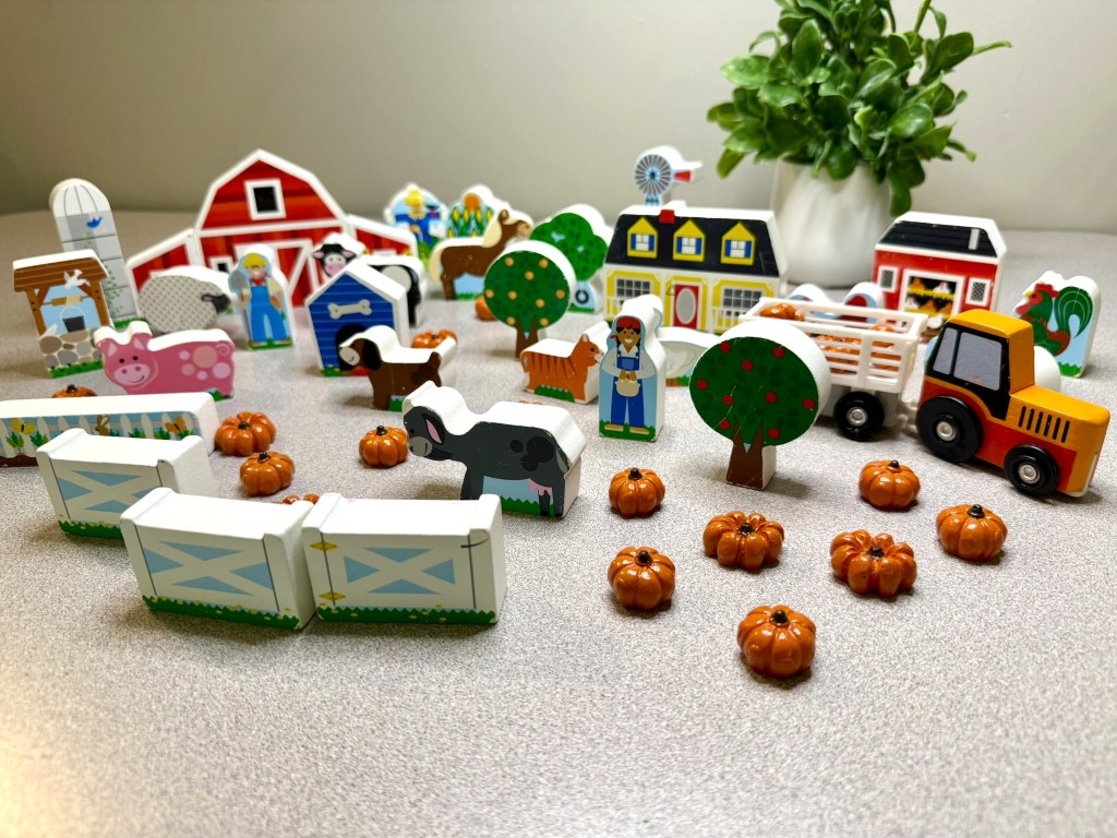 A colorful wooden farm set featuring various farm buildings, animals, trees, and pumpkins on a gray surface.