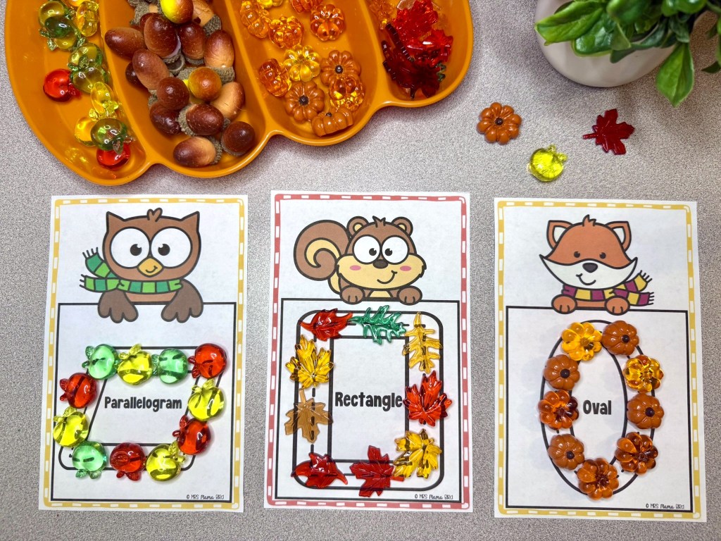 Three educational cards displaying different geometric shapes: 'Parallelogram' with colorful plastic shapes, 'Rectangle' decorated with leaves, and 'Oval' surrounded by flower shapes. A tray of assorted plastic beads is on the left.