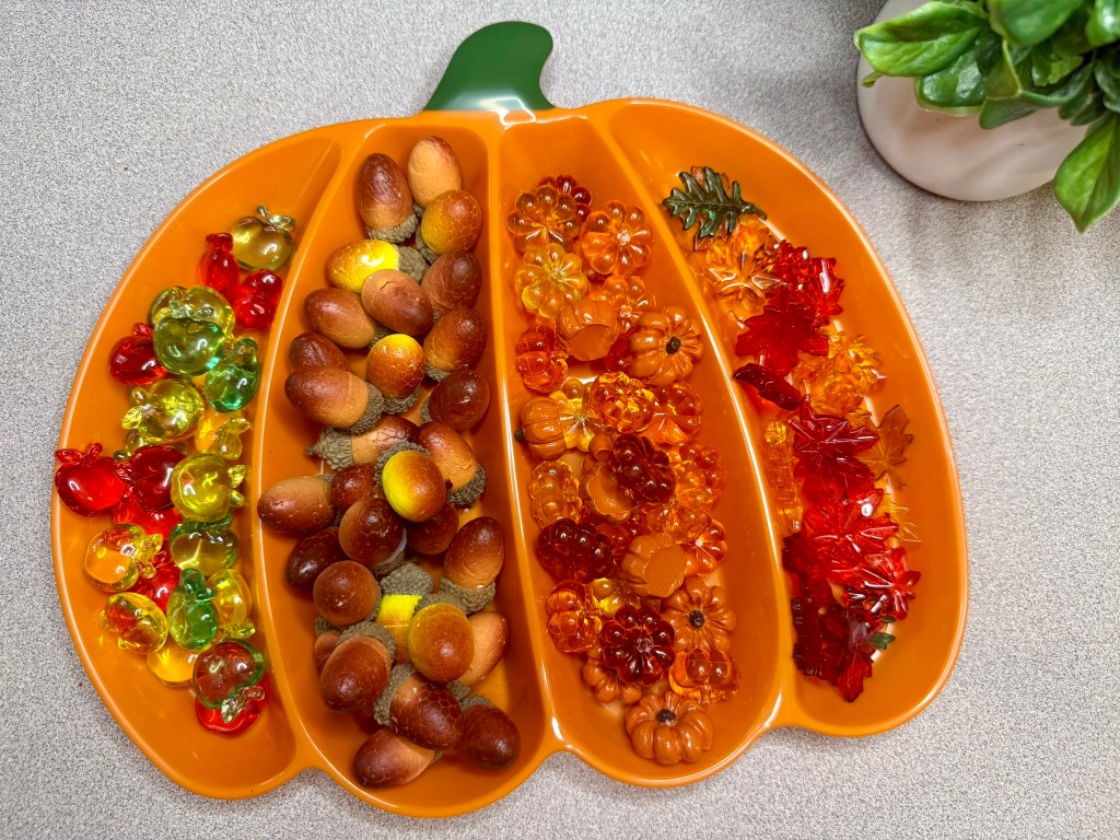 An orange pumpkin-shaped platter filled with colorful candy and decorations, including green and red gummy bears, acorn-shaped candies, and assorted autumn-themed gummies like leaves and pumpkins.